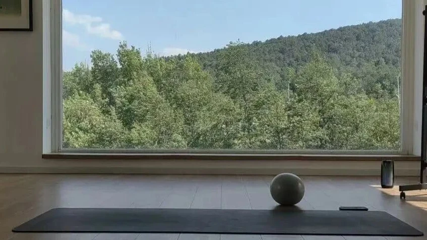 Mountain forest behind a window of a somatic room with yoga mat on the floor