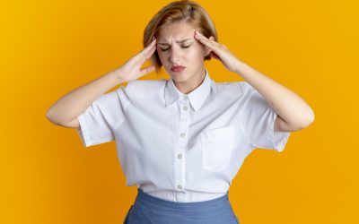 young tired blonde russian girl holds head isolated on orange background with copy space